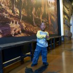Dr. Gillespie's son in front of a dinsoaur mural